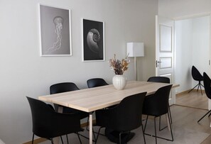 Un espace repas moderne avec une table rectangulaire, des chaises noires et deux œuvres d’art encadrées accrochées au mur.