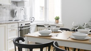 A modern kitchen with white cabinets, a wooden table set for dining, and a window with a view of buildings. - 2ndhomes Central 85m2 2BR Apartment (Helsinki)
