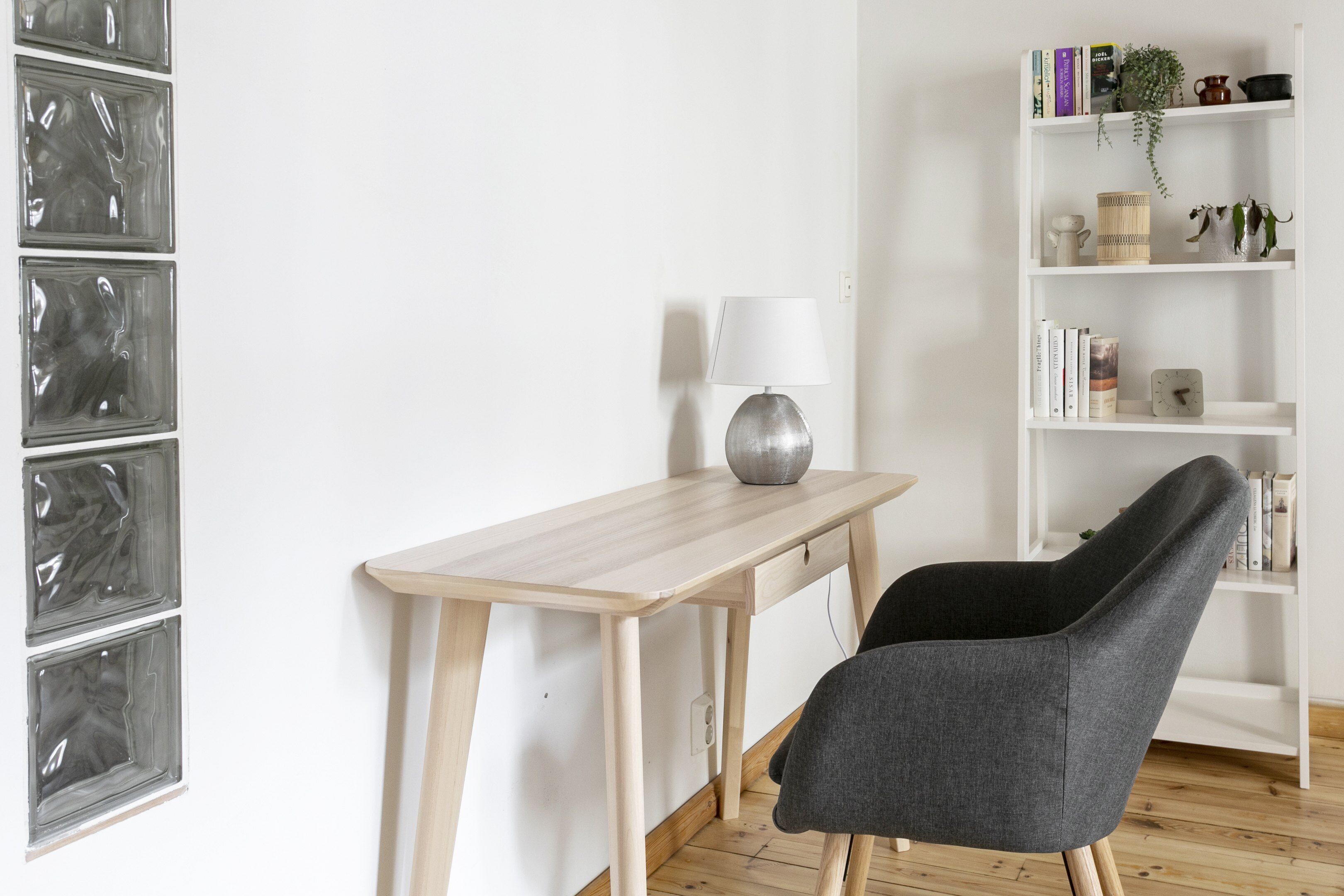 A room with a wooden desk, a grey chair, a white bookshelf, and a wall with four framed pictures.