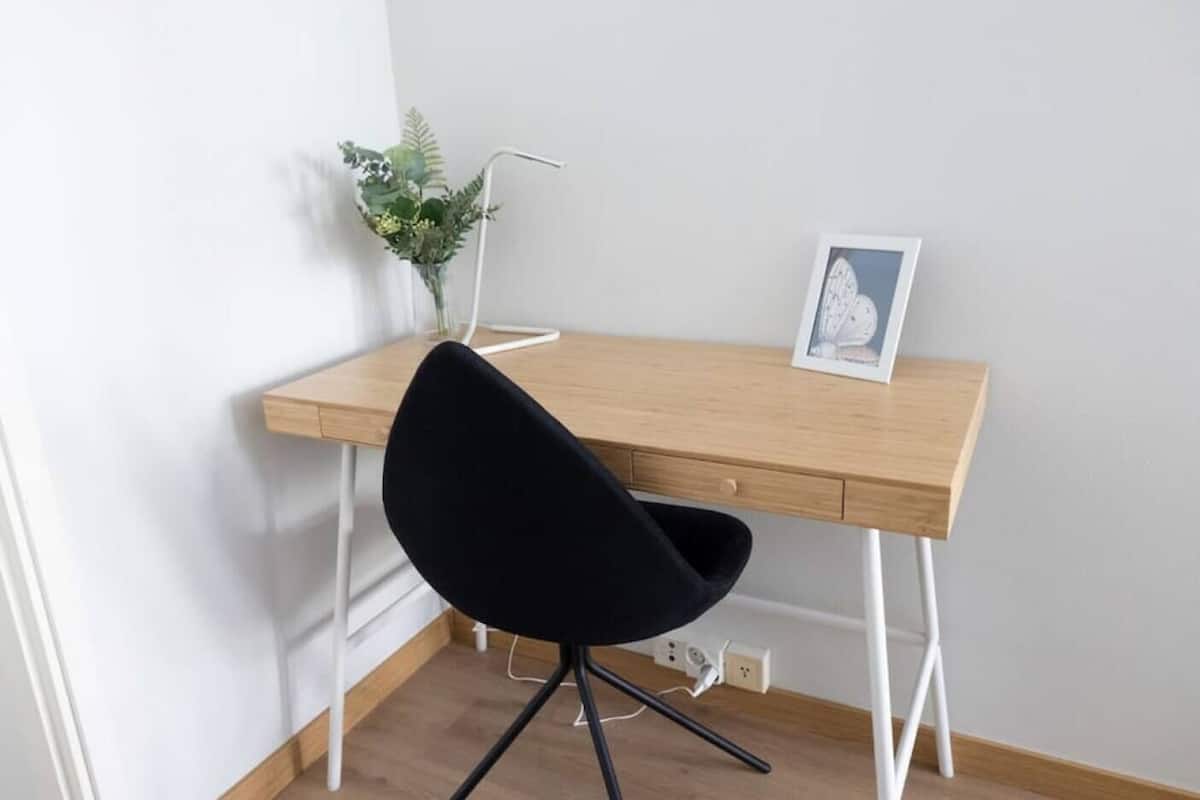 Un bureau en bois, une chaise noire, une petite plante et un tableau encadré posés sur le bureau.