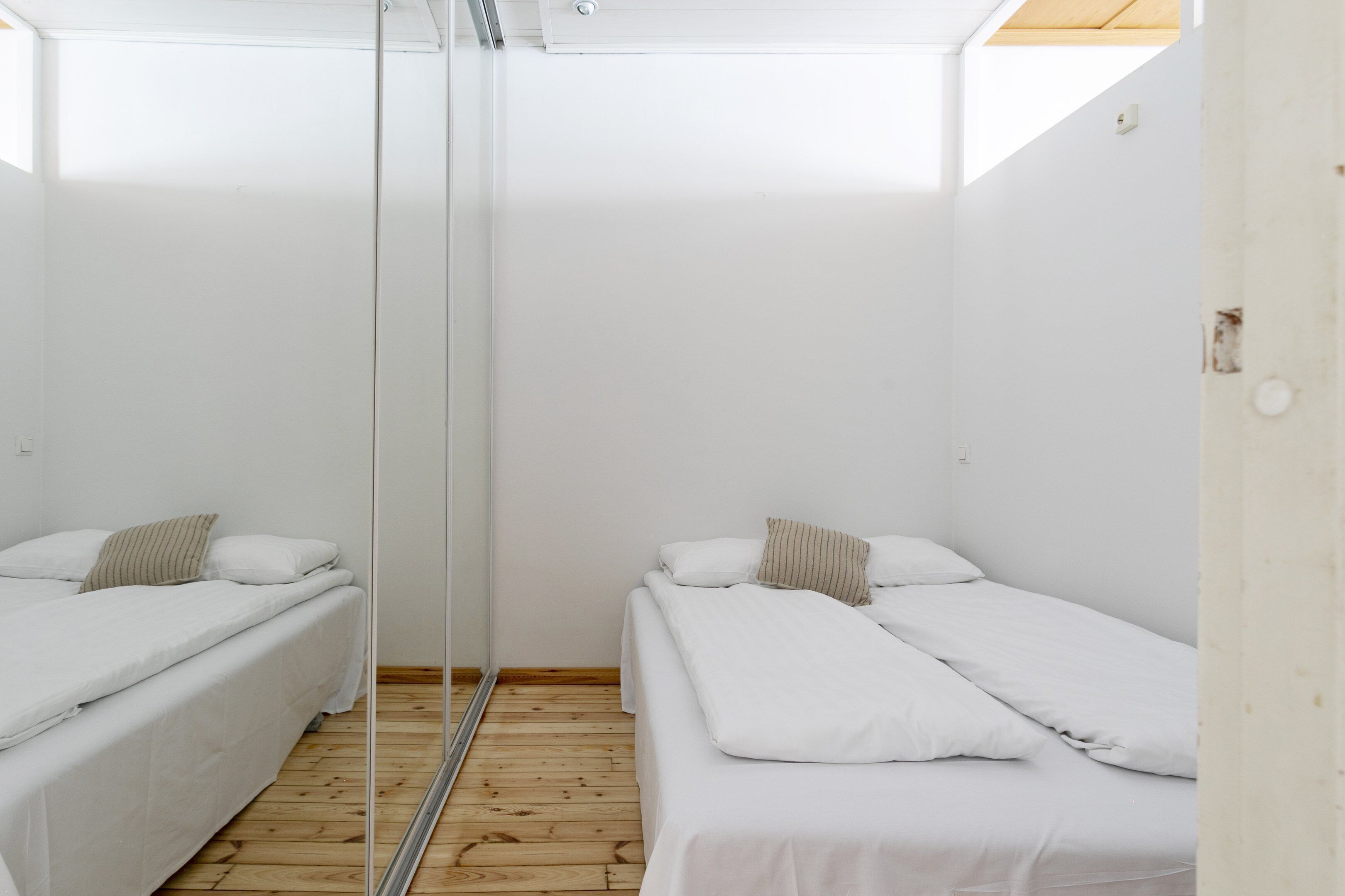Una habitación con dos camas individuales, suelo de madera y un espejo grande.