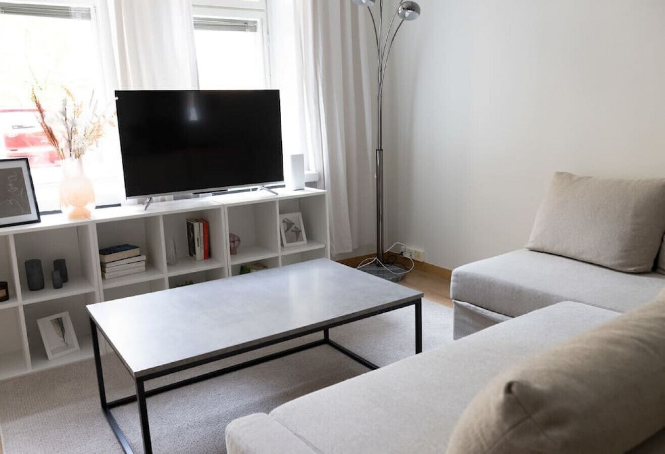 A modern living room with a flat-screen TV, a white sofa, a coffee table, and a bookshelf.