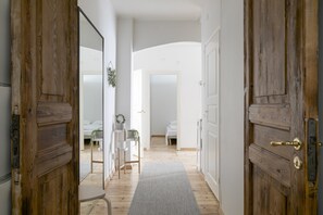 A hallway with wooden doors leading to a bedroom with a bed and a bedside table.