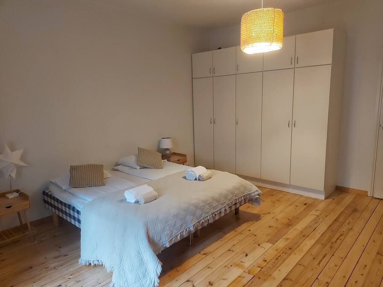 Une chambre à coucher comprenant un lit, une table de chevet, une lampe, une armoire et un luminaire suspendu.