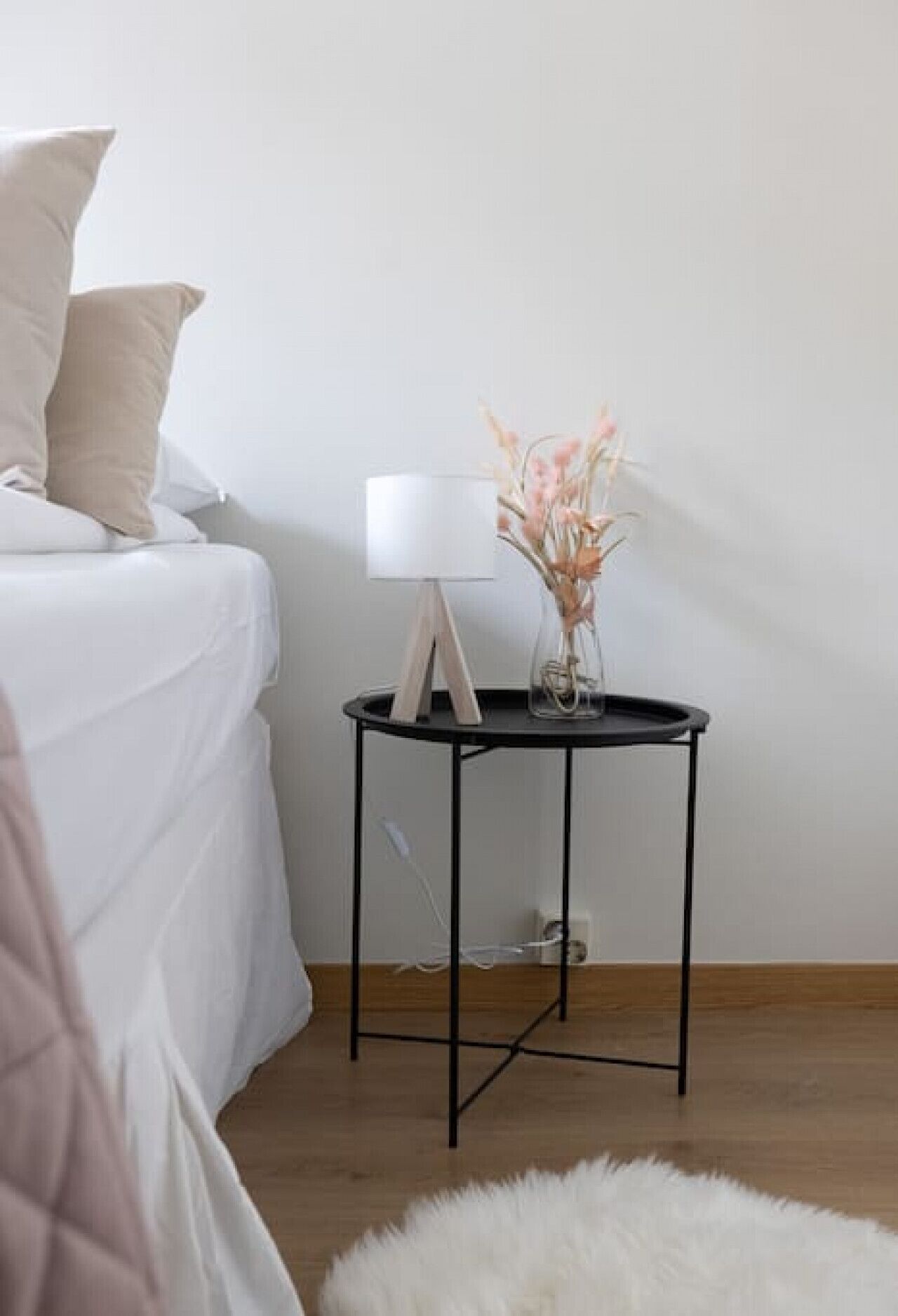 A bedroom with a bed, a bedside table with a lamp, and a vase with flowers.