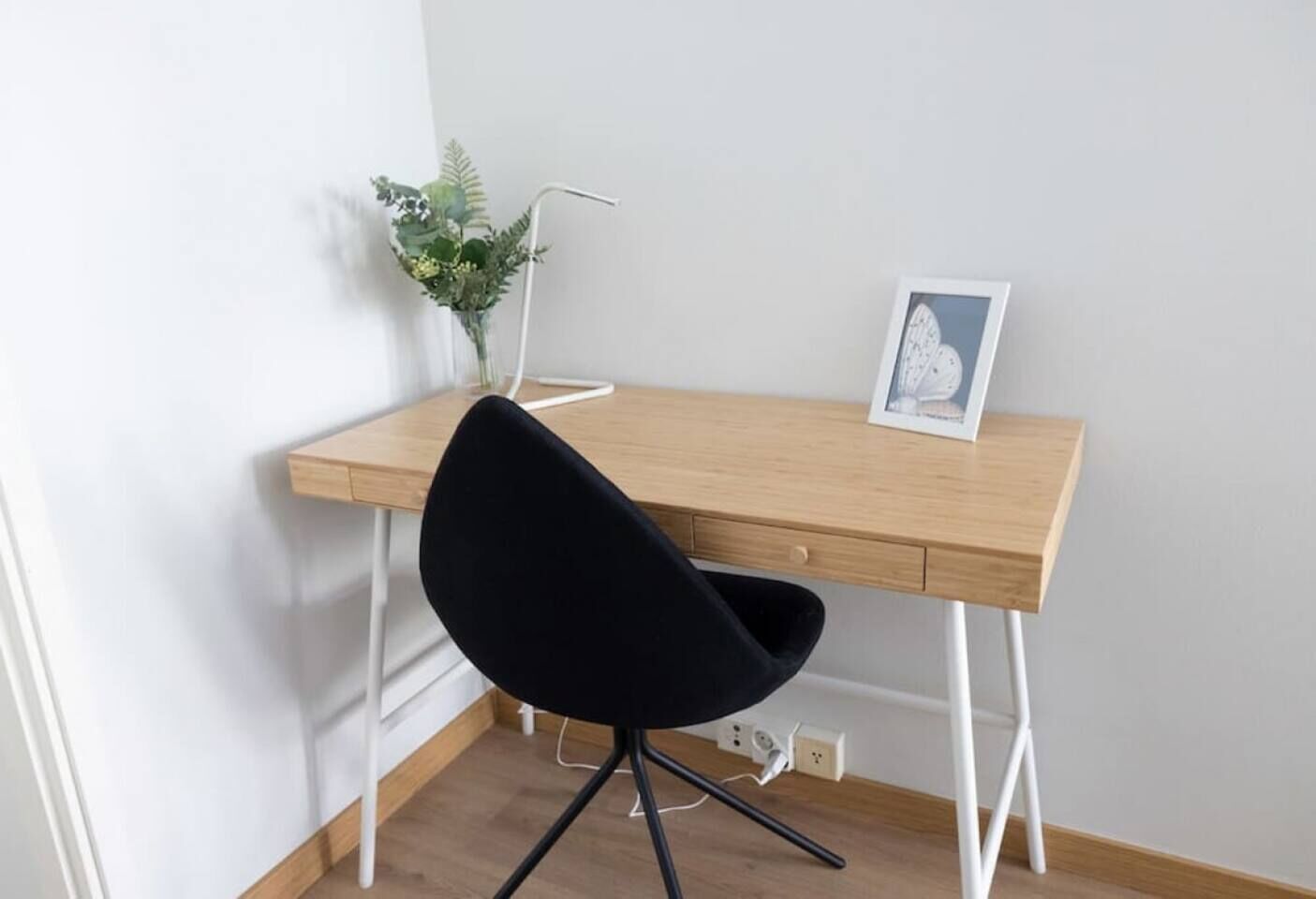 Un bureau en bois, une chaise noire, une petite plante et un tableau encadré posés sur le bureau.