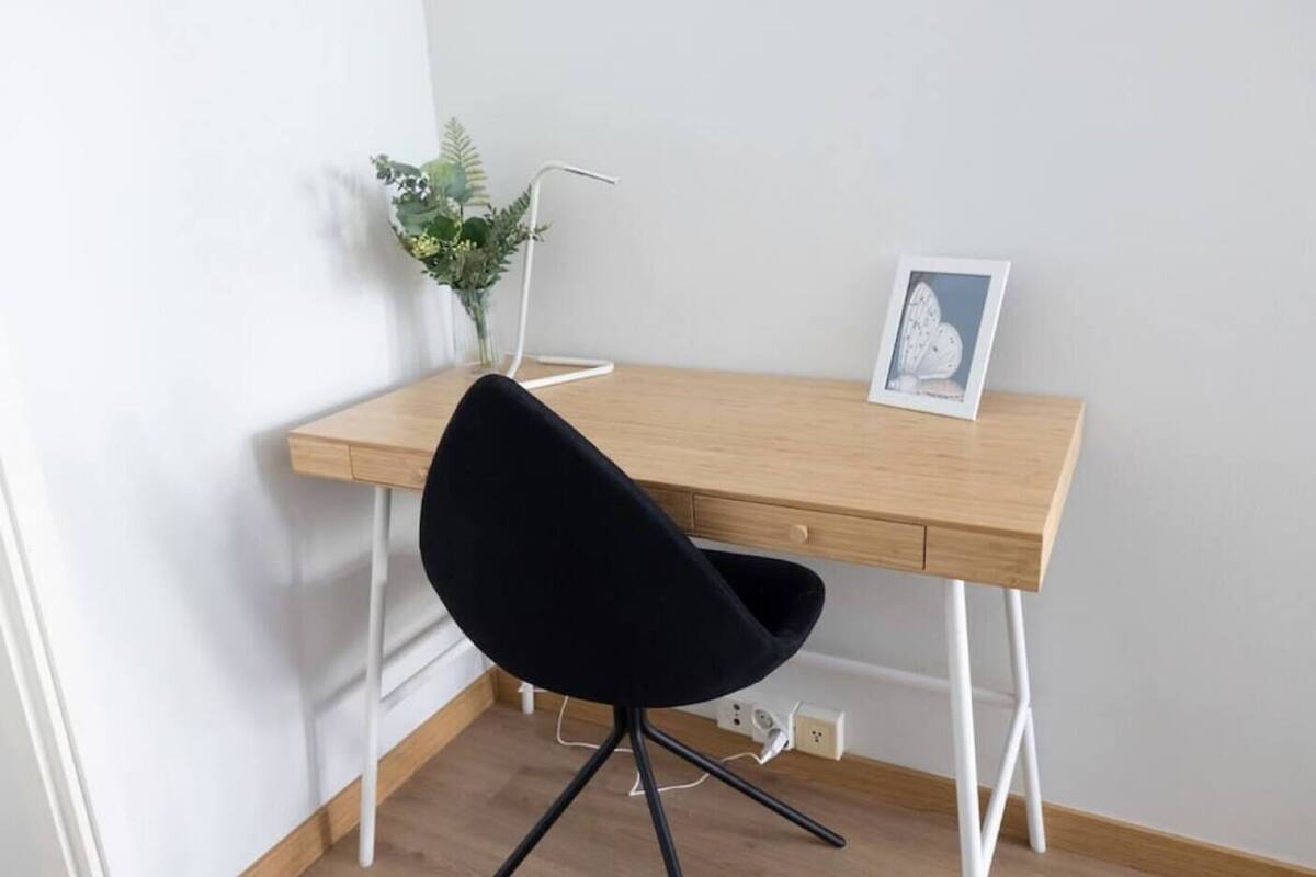 Un bureau en bois, une chaise noire, une petite plante et un tableau encadré posés sur le bureau.