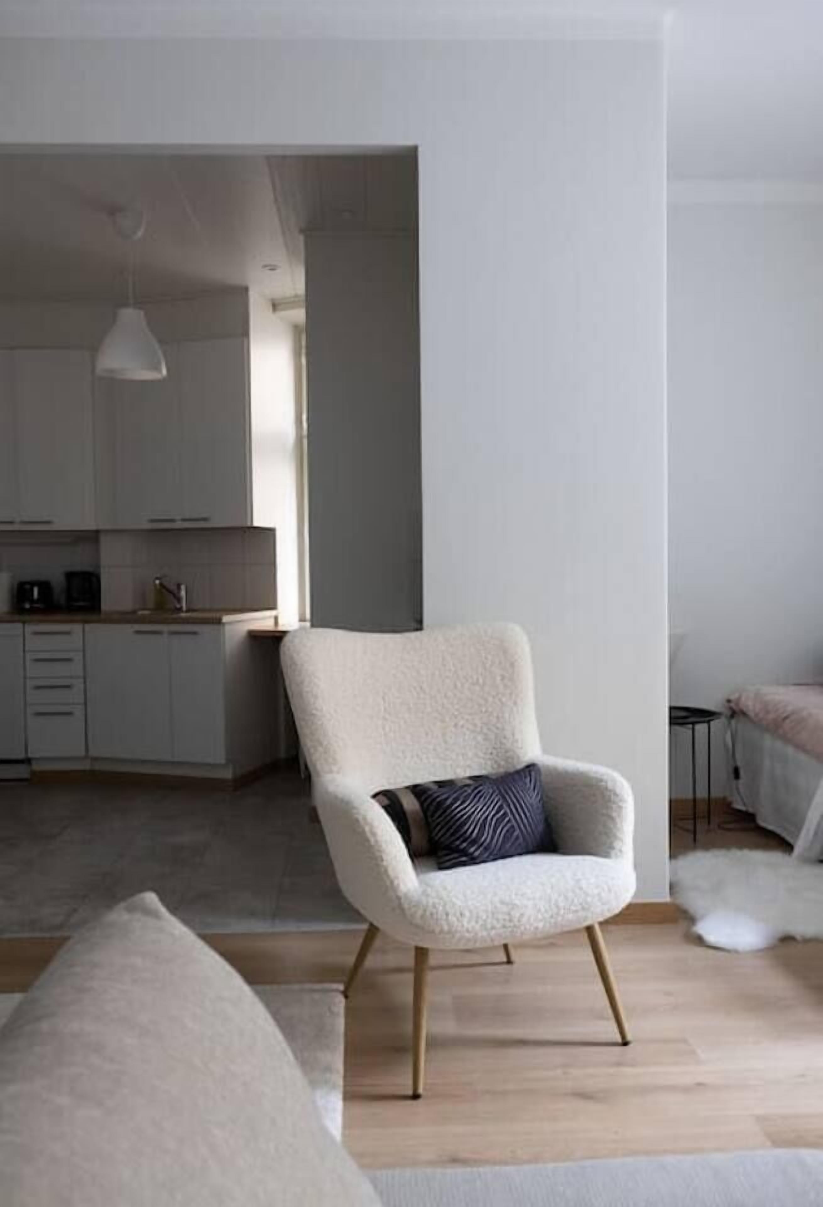 Ett modernt vardagsrum med en ljusfärgad fåtölj, en soffa och ett kök i bakgrunden.