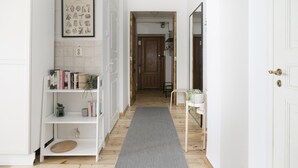 A hallway with a white bookshelf, a framed botanical print, and a grey rug leading to a door. - 2ndhomes Central 85m2 2BR Apartment (Helsinki)