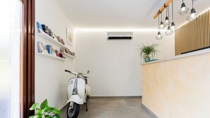 Un espace d’accueil avec un scooter blanc, une plante en pot et des étagères remplies de livres.