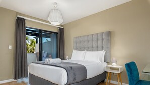 A modern bedroom with a large bed, a nightstand, a chair, and a view through a glass door to the outside. - Knightsbridge 108 (Cape Town)
