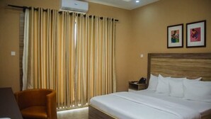 Habitació d'hotel amb un llit, una cadira, una tauleta de nit i cortines.