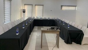 Una sala de conferències amb una taula llarga, cadires blanques i ampolles d'aigua.