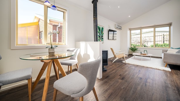 Un salon moderne avec une table à manger en verre, des chaises recouvertes d’un tissu gris, un canapé et une cheminée.