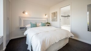 Une chambre avec un grand lit, une table de chevet, une commode, un luminaire fixé au mur et une vue sur une salle de bain avec une baignoire.