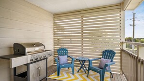 Un balcon avec un barbecue, deux chaises et un tapis jaune et blanc à motifs chevrons.