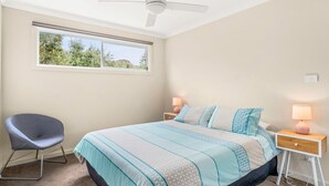 Une chambre à coucher comprenant un lit, une chaise, une table de chevet, une lampe et un ventilateur de plafond.