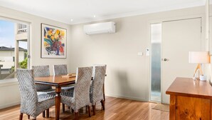 Un coin repas avec une table en bois et des chaises à motifs, un tableau accroché au mur et un appareil de climatisation au-dessus.