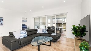 Ein modernes Wohnzimmer mit einer Eckcouch, einem Glastisch und einem Essbereich, der durch Glastüren sichtbar ist.