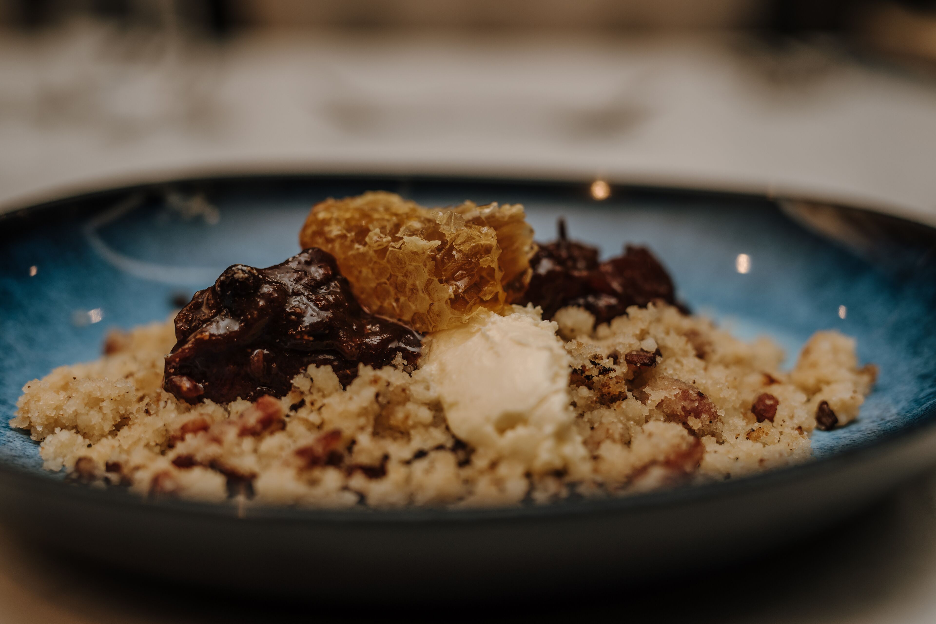 Primer plano de un plato de postre con una porción de helado, panal y frutas secas.