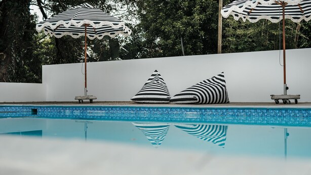 A swimming pool with two striped umbrellas and two striped pillows on the edge. - The Hawthorn Boutique Hotel (George)