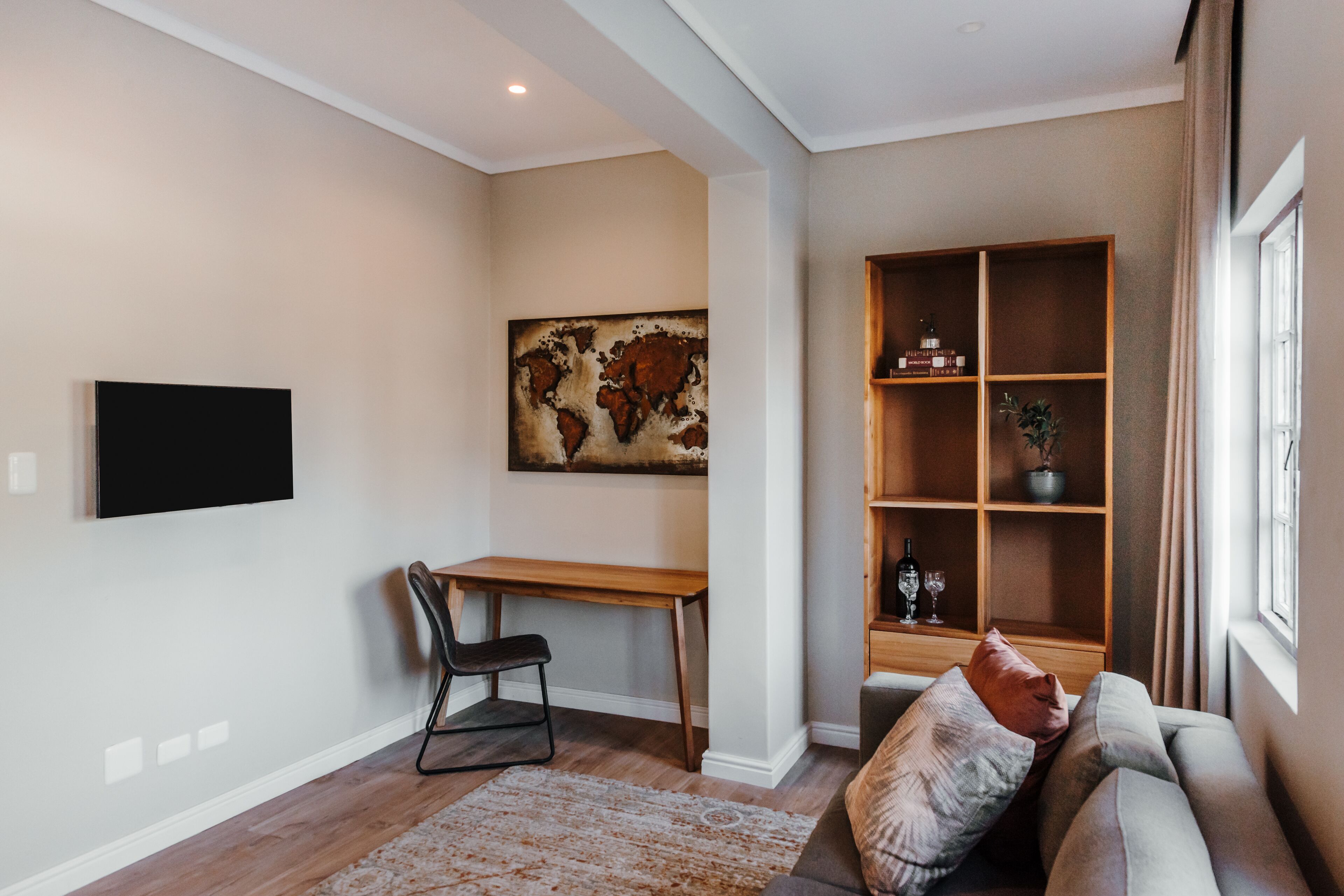 En moderne stue med et træskrivebord, en behagelig sofa, et fladskærms-tv på væggen og en reol med dekorative genstande.