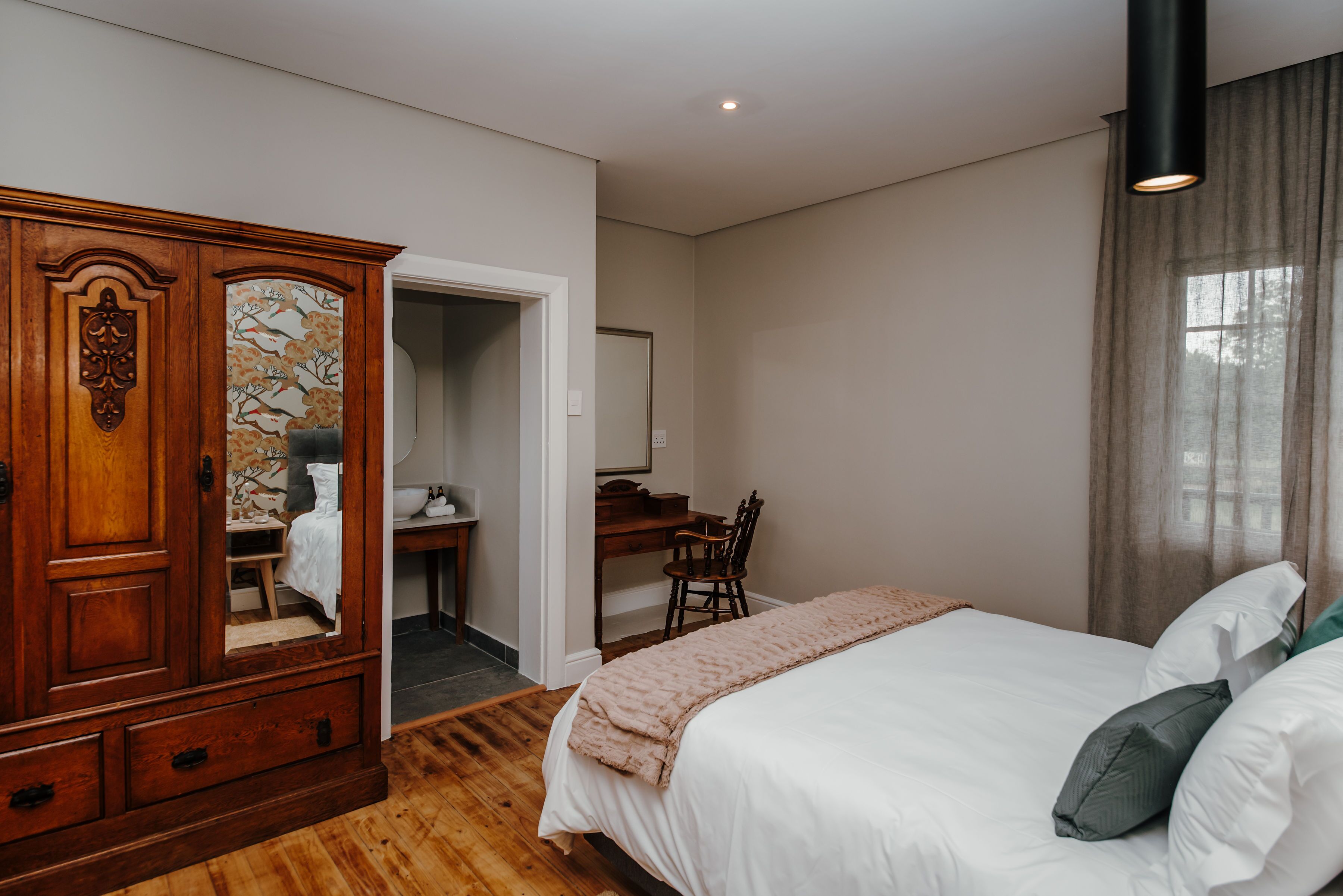 A bedroom with a wooden wardrobe, a desk, and a bed with pillows.
