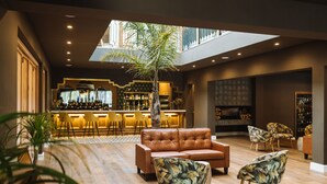 A spacious lounge area with a leather sofa, patterned armchairs, a central tree, and a bar with shelves of bottles. - The Hawthorn Boutique Hotel (George)