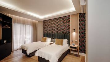 A modern hotel room with two beds, a wardrobe, a desk, and a patterned wallpaper.