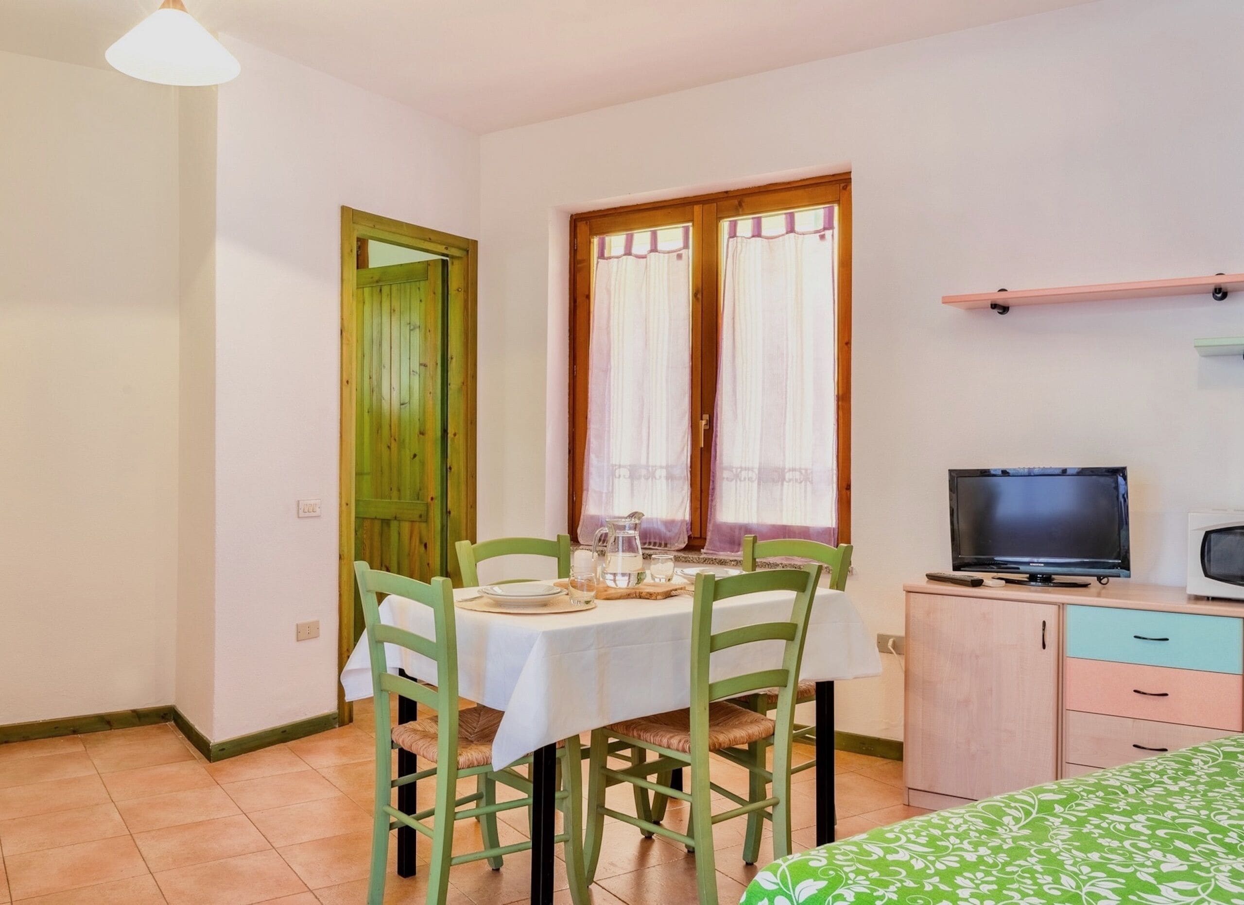 A small, clean room with a dining table set for two, a television, and a cabinet.