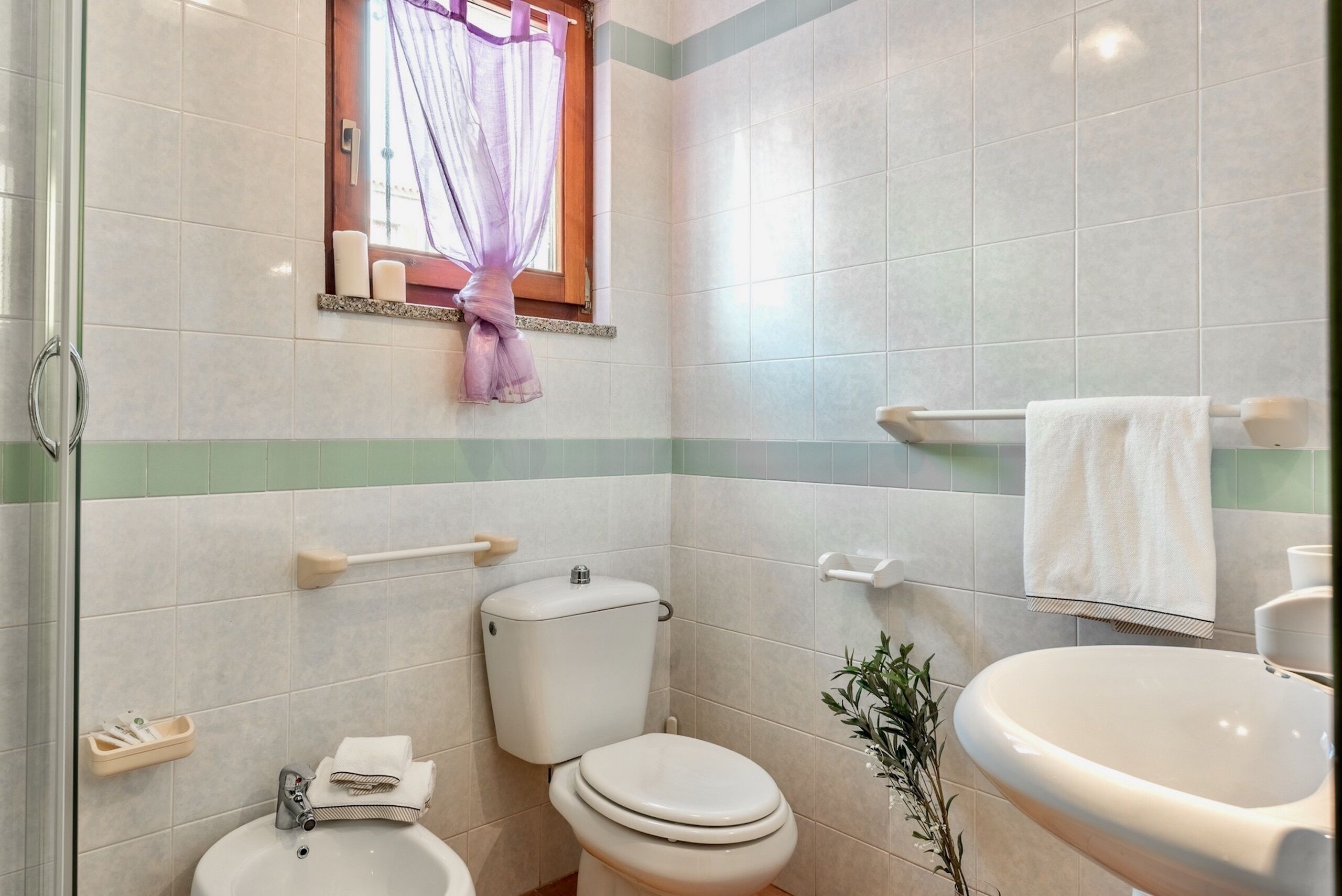 Un baño con inodoro, lavamanos y ventana con cortina.