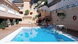 A swimming pool with a clear blue water, surrounded by a building with balconies and a white fence. - Apartment - LOS GIGANTES (Santiago del Teide)