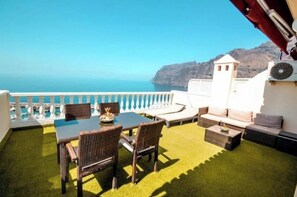 A terrace with a table and chairs, a sofa, and a view of the sea and mountains.