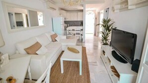 A modern living room with a white sofa, a coffee table, a TV, and a kitchen in the background. - Apartment - LOS GIGANTES (Santiago del Teide)