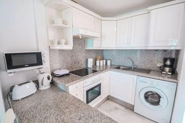 A compact kitchen with white cabinets, a microwave, toaster, sink, and a washing machine.