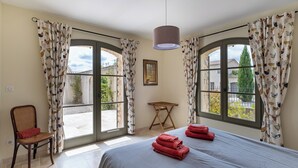 A bedroom with two beds, a chair, and a table. - Spacious, comfortable stone farmhouse with swimming pool for 8 people in Uzès (GARRIGUES STE EULALIE)