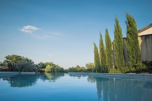 A clear swimming pool with a calm water surface, surrounded by tall, slender trees and a variety of shrubs. - Spacious, comfortable stone farmhouse with swimming pool for 8 people in Uzès (GARRIGUES STE EULALIE)