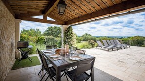 An outdoor patio with a table set for dining, a grill, and lounge chairs. - Spacious, comfortable stone farmhouse with swimming pool for 8 people in Uzès (GARRIGUES STE EULALIE)