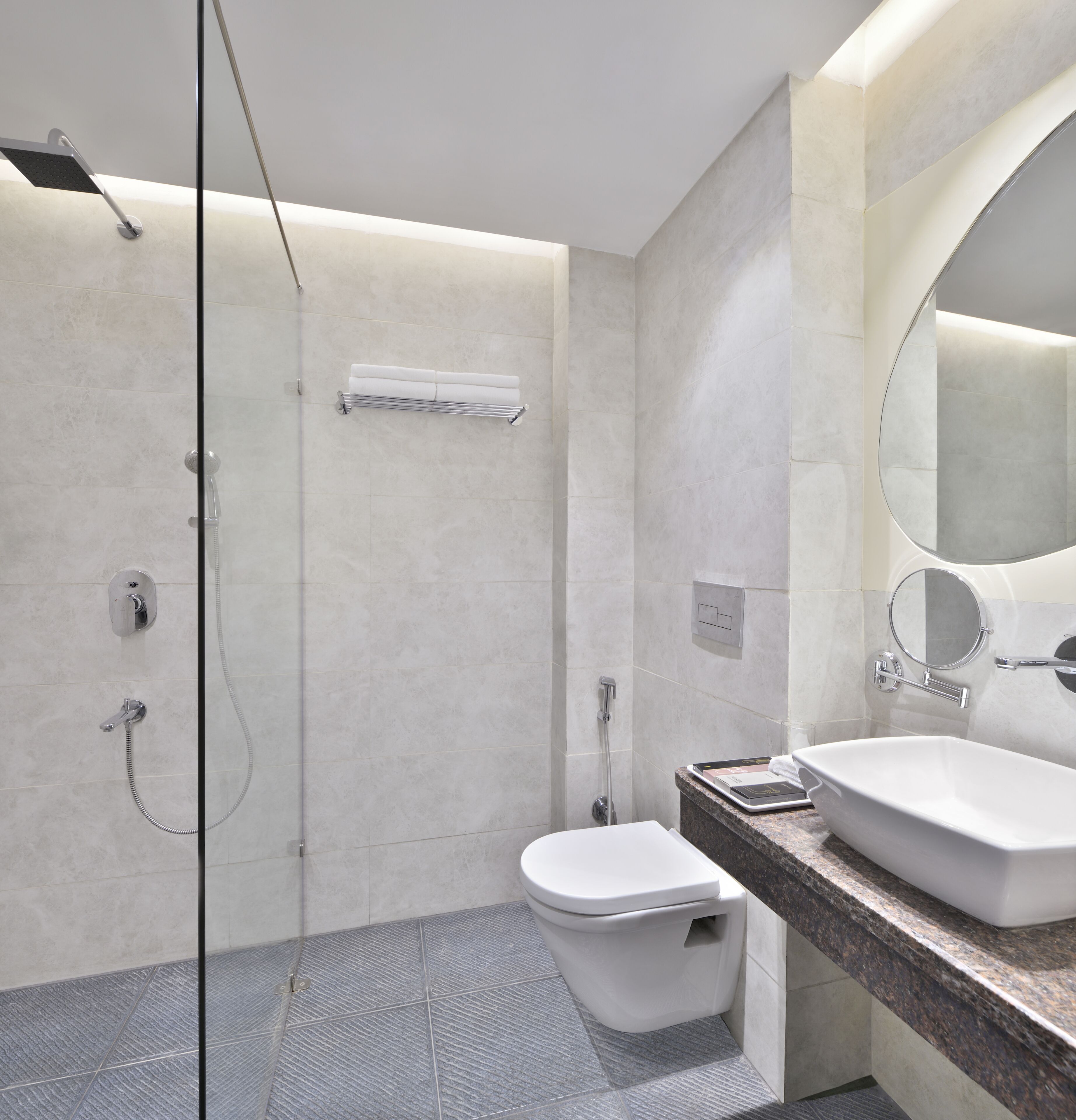 Un bany modern amb una dutxa de vidre, un vàter i un lavabo amb taulell de marbre.