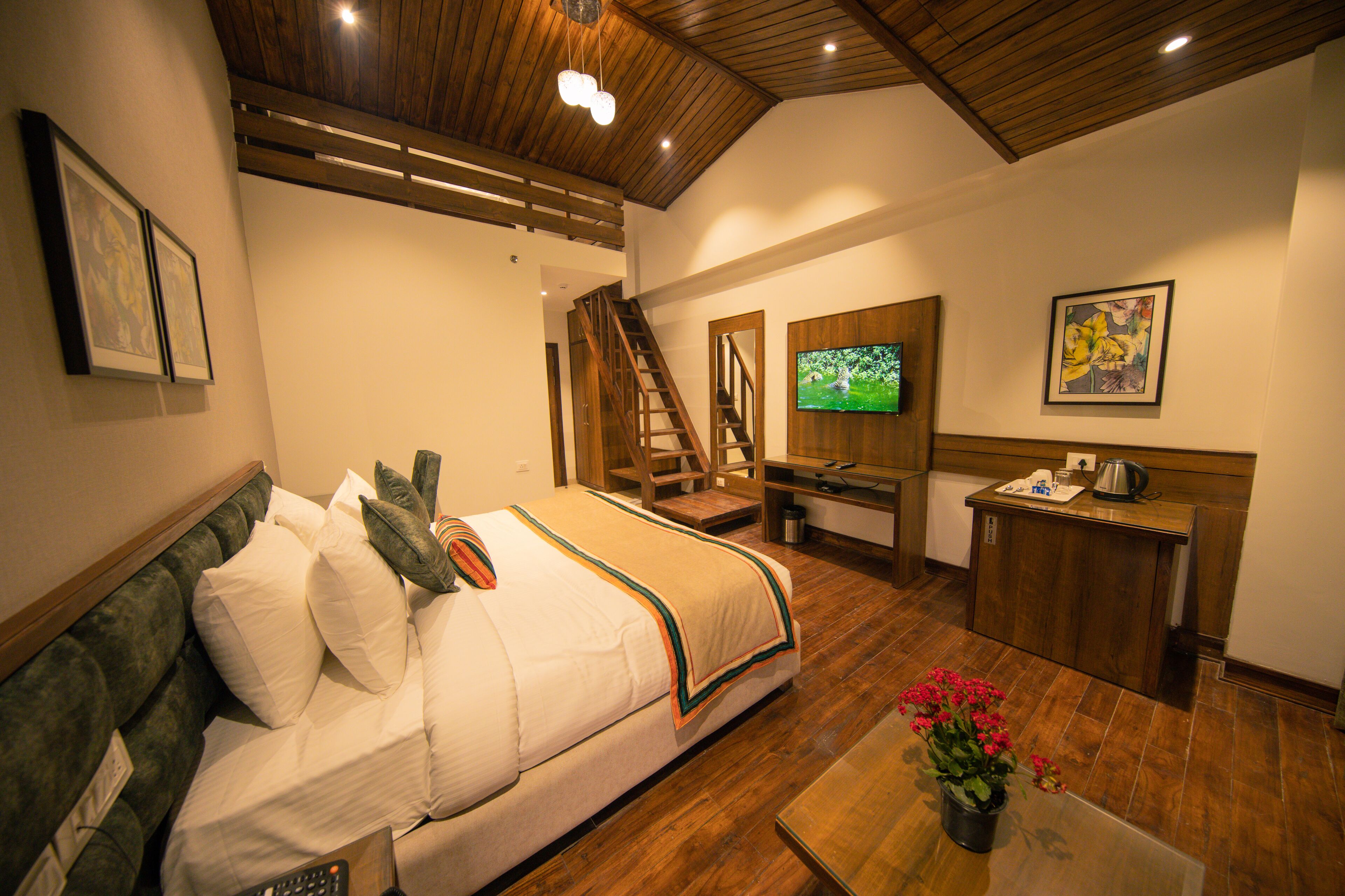 A hotel room with a bed, a coffee table with flowers, a TV, a desk, and a staircase.