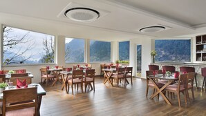 Un comedor amplio con mesas y sillas de madera, ventanas grandes con vistas a la montaña y una zona de bar con taburetes.
