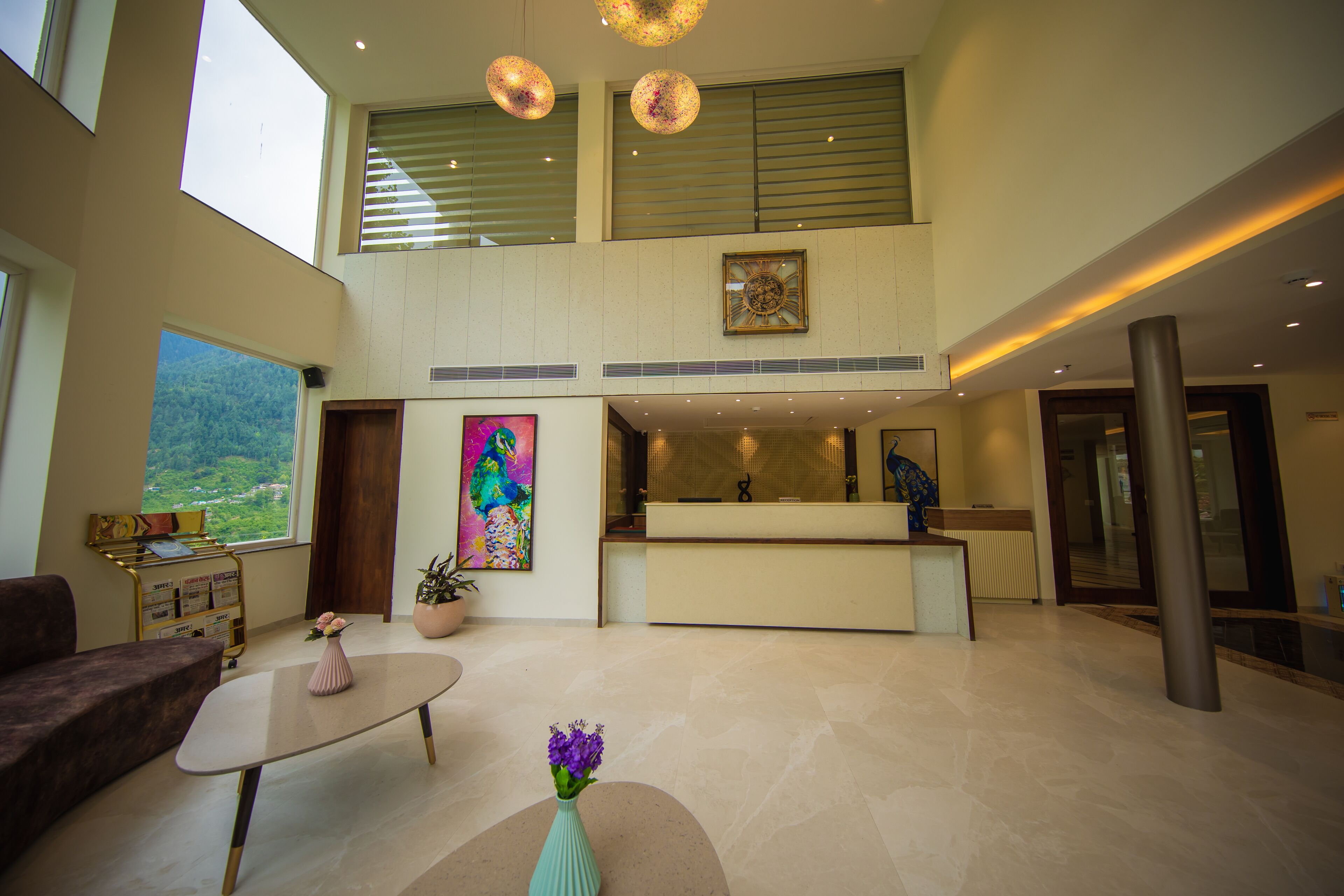 A spacious lobby with a reception desk, a coffee table with a vase of flowers, and a large window offering a view of greenery.