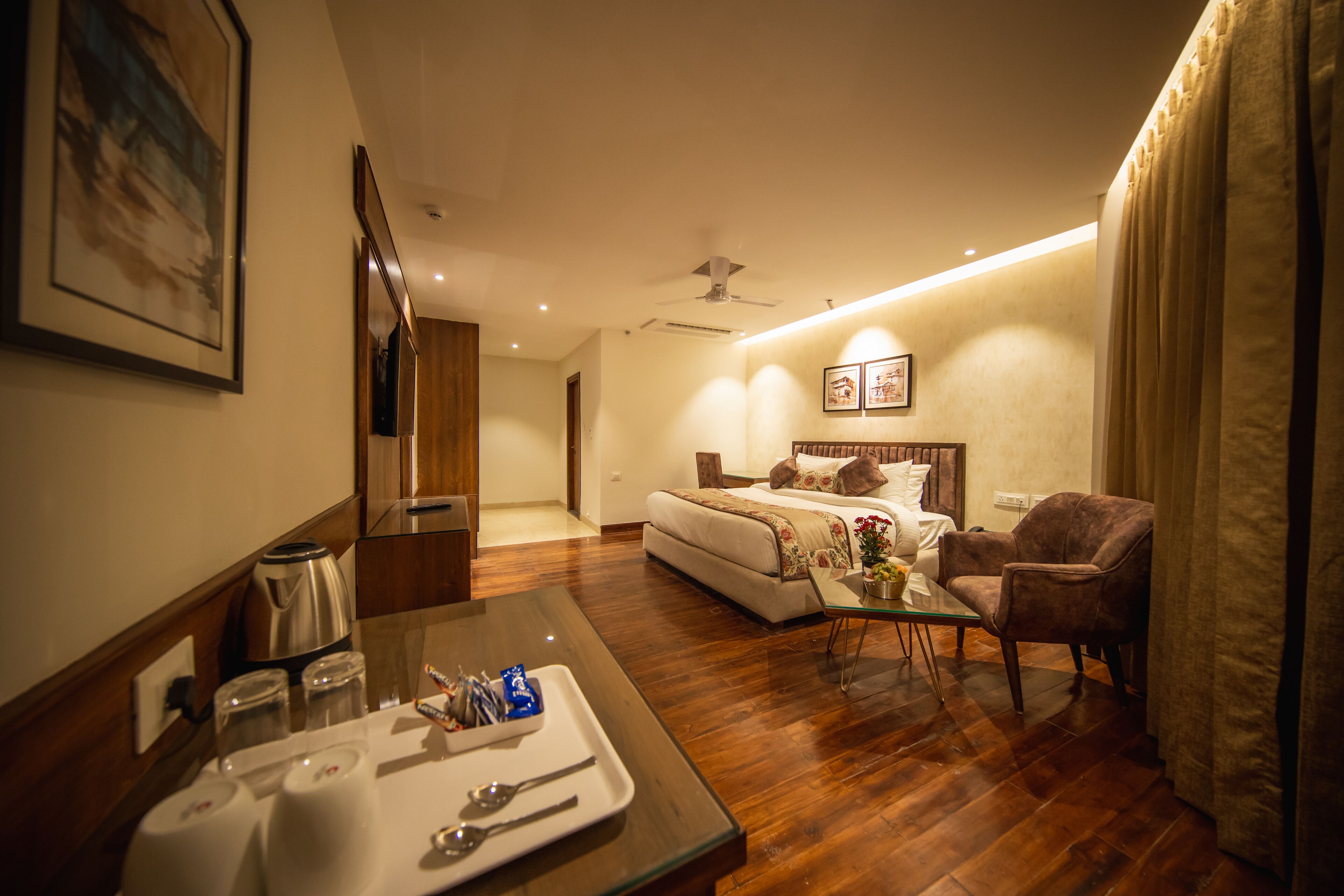 A hotel room with a bed, a sitting area with a table and chairs, a coffee maker, and a tray with breakfast items.