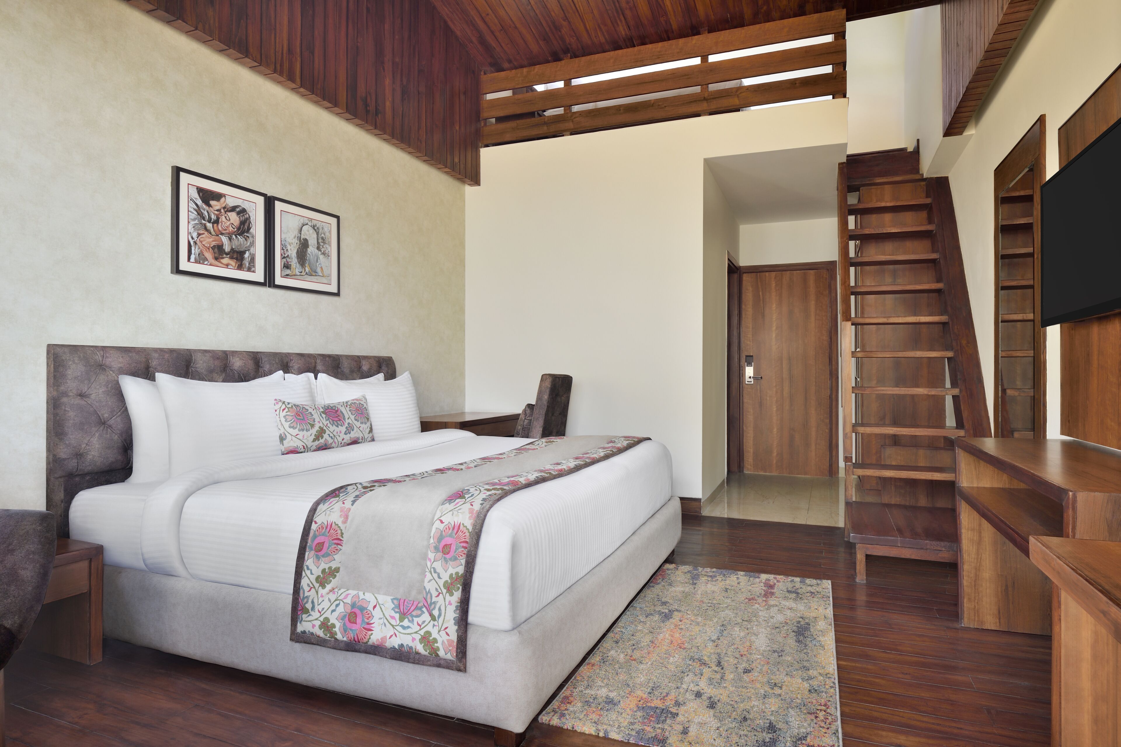 A bedroom with a large bed, wooden headboard, a staircase, and a flat-screen TV.