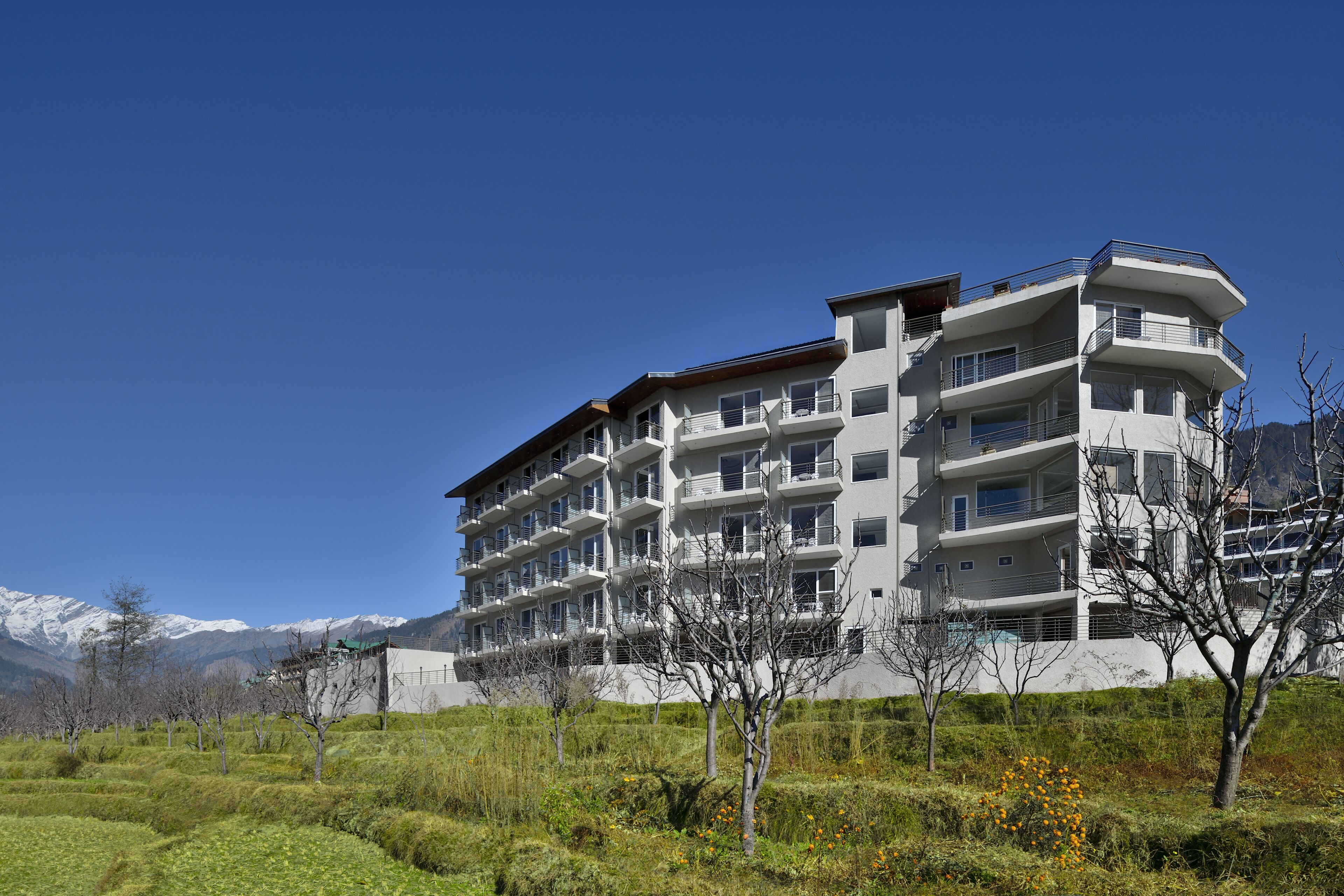 Un hotel de varios pisos con balcones, rodeado de un paisaje con césped y montañas al fondo.
