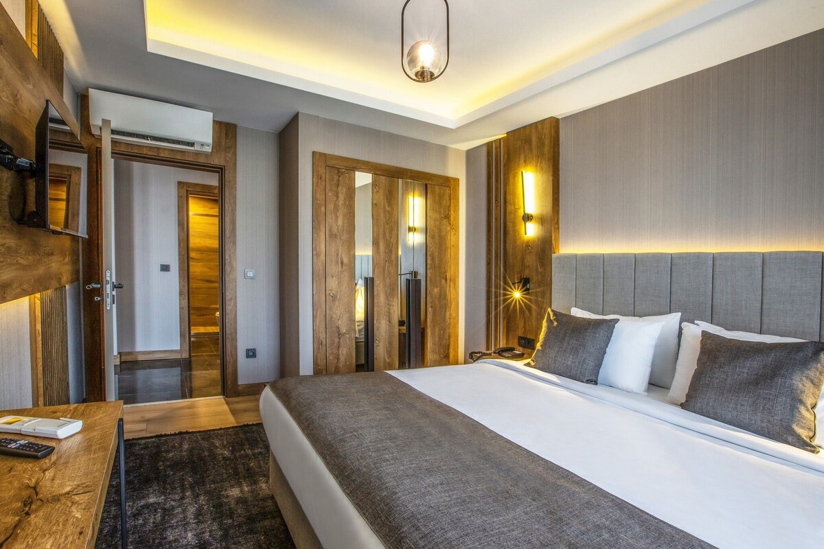 Una habitación de hotel moderna con una cama grande, un armario de madera, un espejo y una lámpara en el techo.