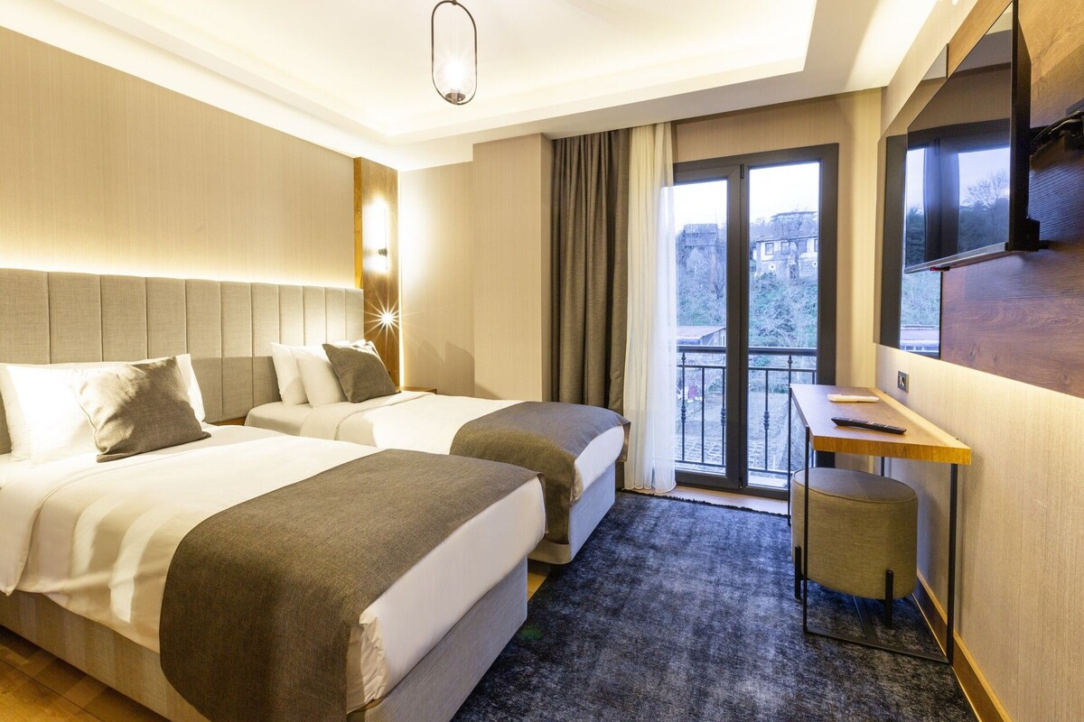 Habitación de hotel con dos camas, un escritorio, televisión y balcón con vistas.