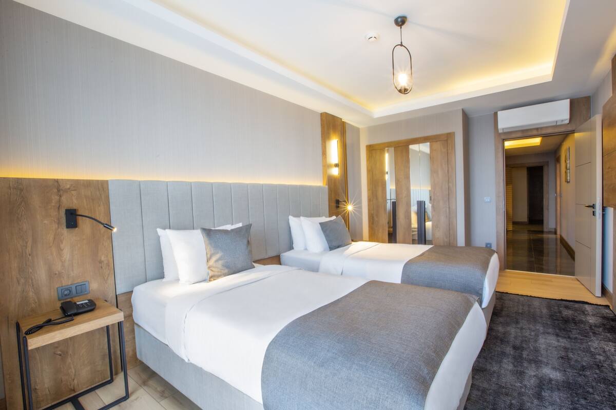 Una habitación de hotel con dos camas, una mesita de noche, una lámpara y un espejo.