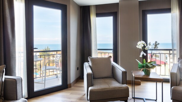 Quarto de hotel moderno com varanda, sofá, uma pequena mesa com um vaso e vista para o mar.