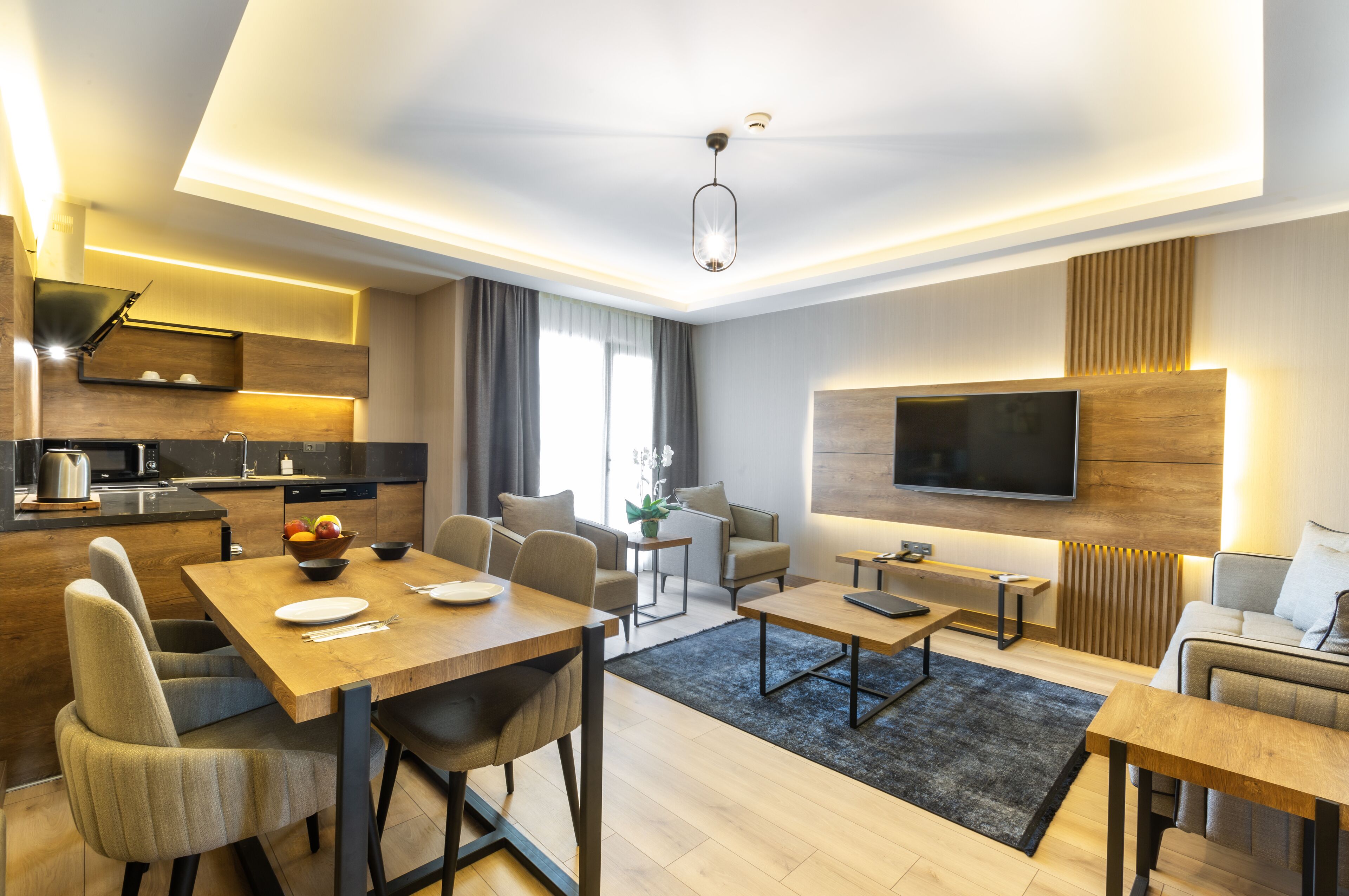 Un salon moderne comprenant un coin repas, une cuisine et un téléviseur fixé au mur.